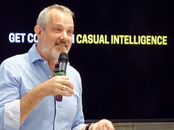 Photo of Josh Clark speaking in front of a screen with the text, "Get cozy with casual intelligence"