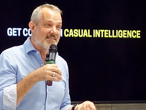 Photo of Josh Clark speaking in front of a screen that says, "Get cozy with casual intelligence"