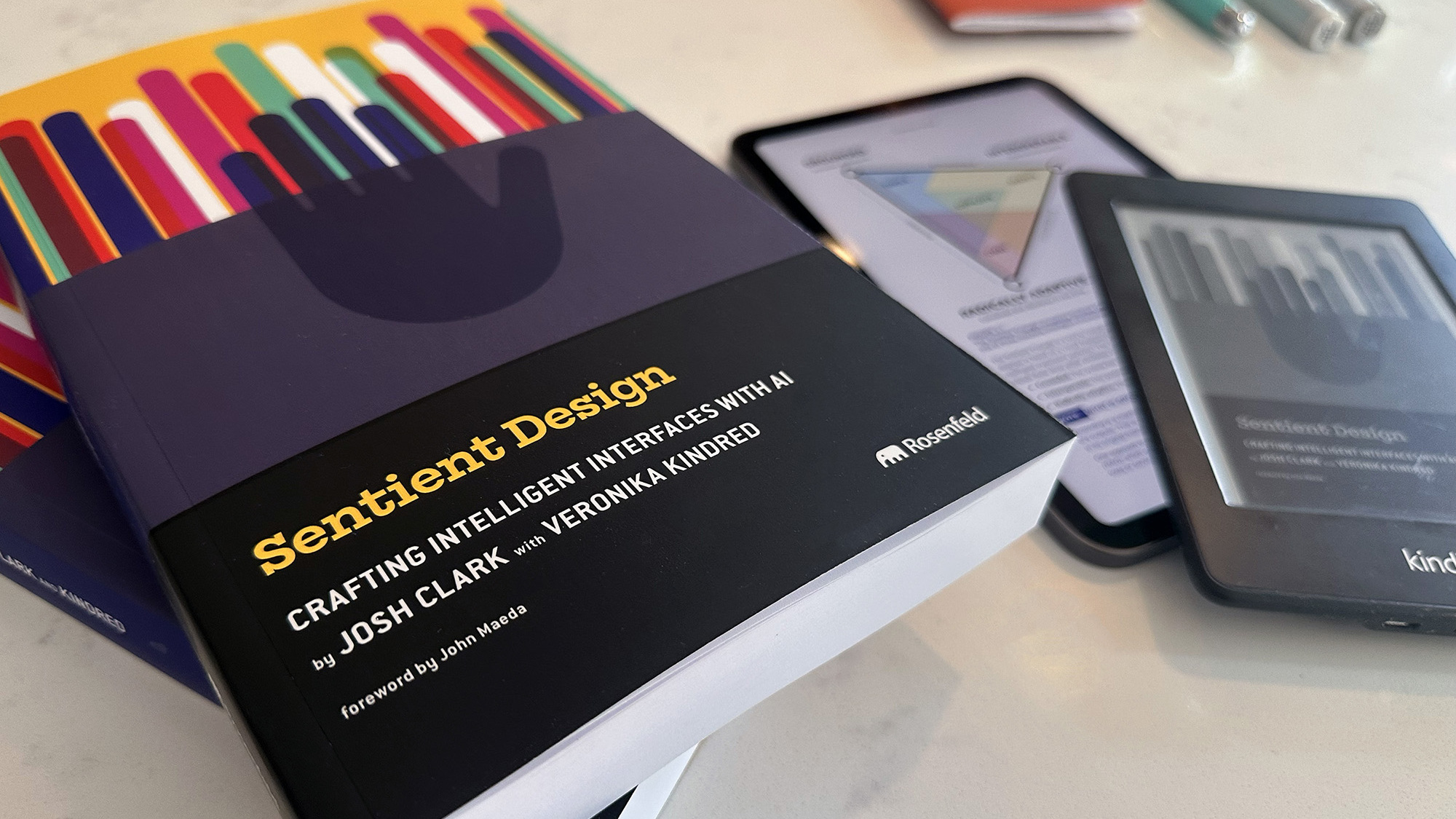 Sentient Design paperbacks next to kindle and ipad editions on a marble surface